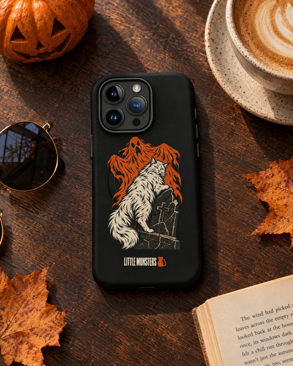 Little Monsters Halloween 2026 graveyard cat iPhone case on a cafe table with a latte and a pumpkin