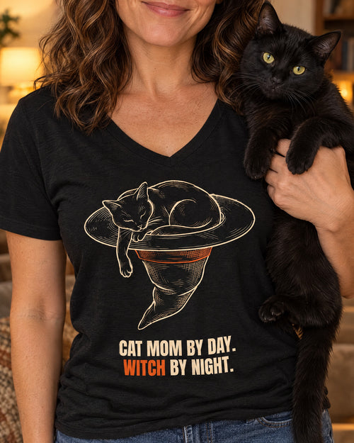 Close-up of the Cat Mom by Day. Witch by Night. V-neck tee: a black cat asleep in a witch hat, worn by a woman holding her black cat