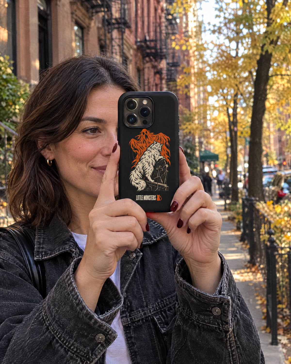 Woman on a New York street holding an iPhone in the Little Monsters Halloween 2026 graveyard cat MagSafe case