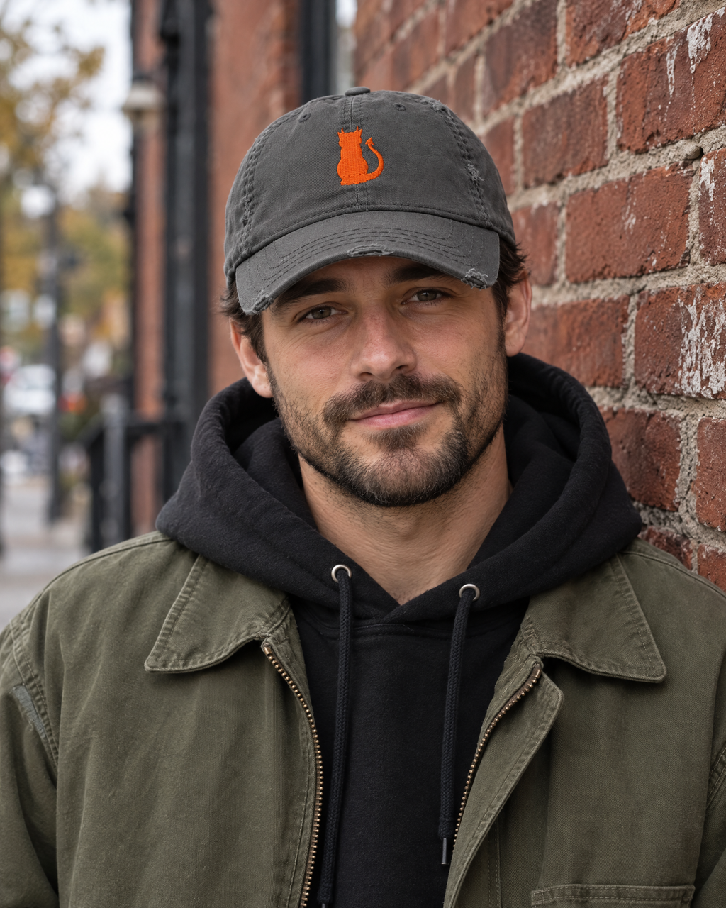 Man in front of a brick wall wearing the charcoal grey Little Monsters devil cat embroidered hat