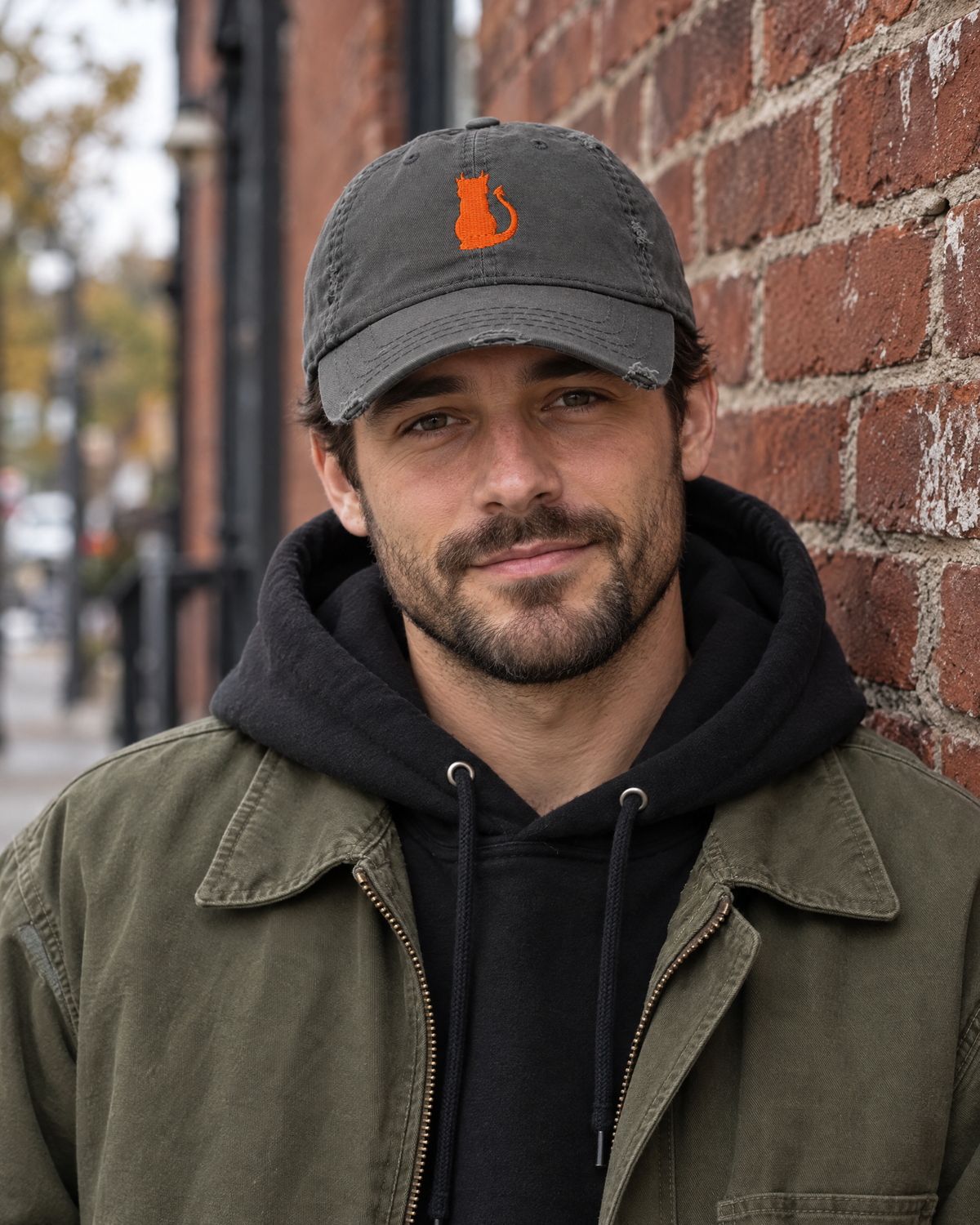 Man in front of a brick wall wearing the charcoal grey Little Monsters devil cat embroidered hat