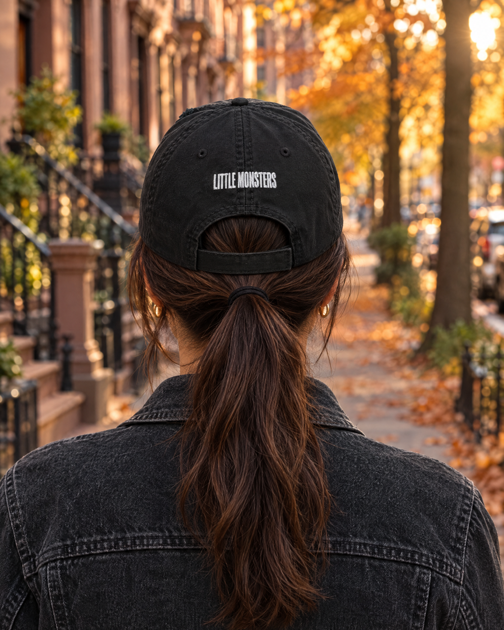 Back of the black Little Monsters hat with LITTLE MONSTERS embroidered above the strap, worn with a ponytail