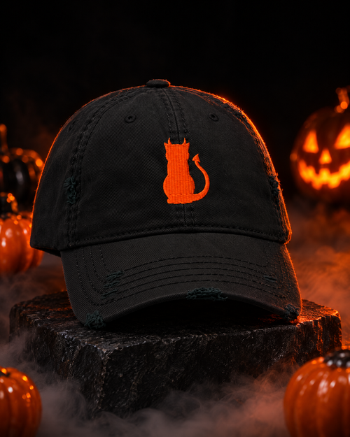 Black Little Monsters devil cat embroidered hat on a stone plinth with glowing jack-o'-lanterns and fog for Halloween