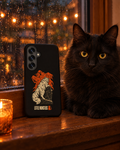 Samsung Galaxy phone in the Little Monsters Halloween graveyard cat case on a rainy windowsill beside a real black cat