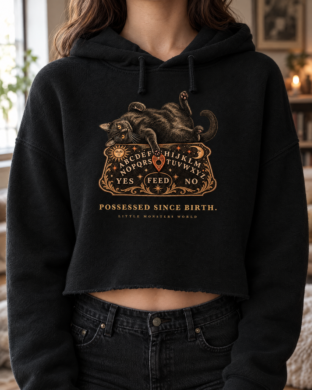 Close-up of the Possessed Since Birth print on the black cropped hoodie: a black cat on a spirit board in gold and copper
