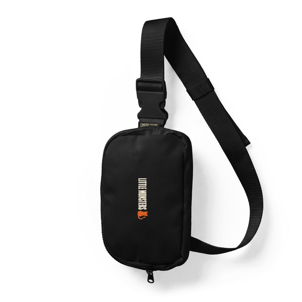 Black Little Monsters logo sling bag with a cream vertical wordmark and an orange devil cat